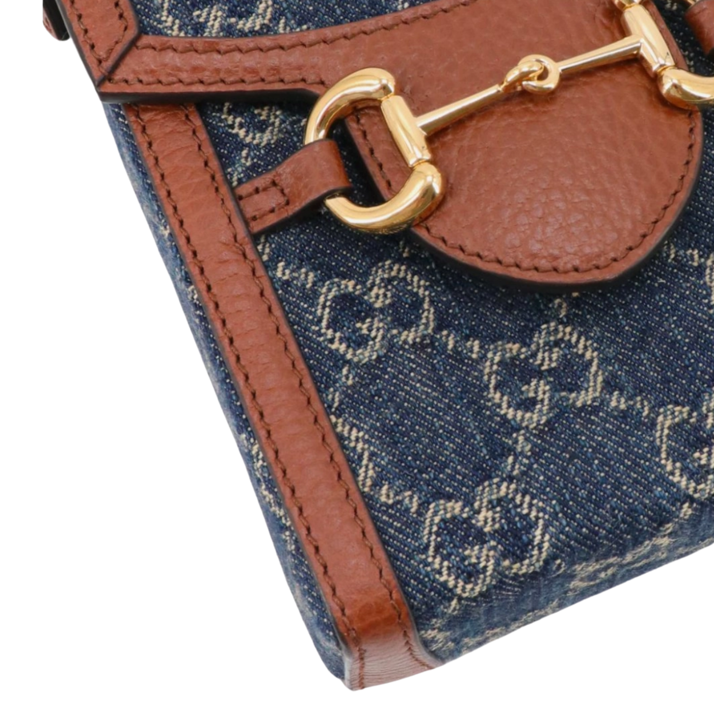 Close-up of a Gucci denim handbag with brown leather strap and gold Horsebit buckle