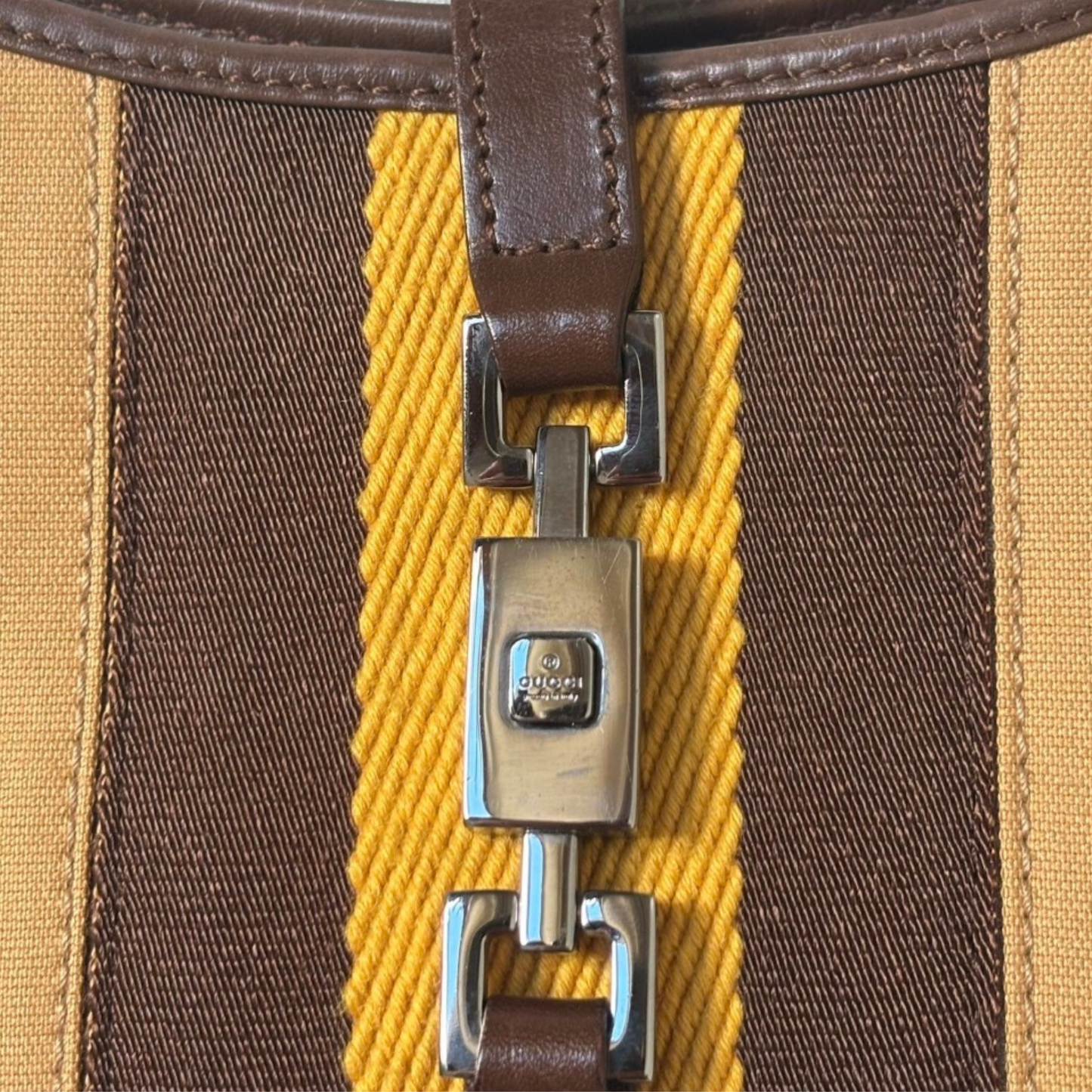 Close-up of a brown and yellow strap with a metal buckle on a textured surface showing Gucci logo.