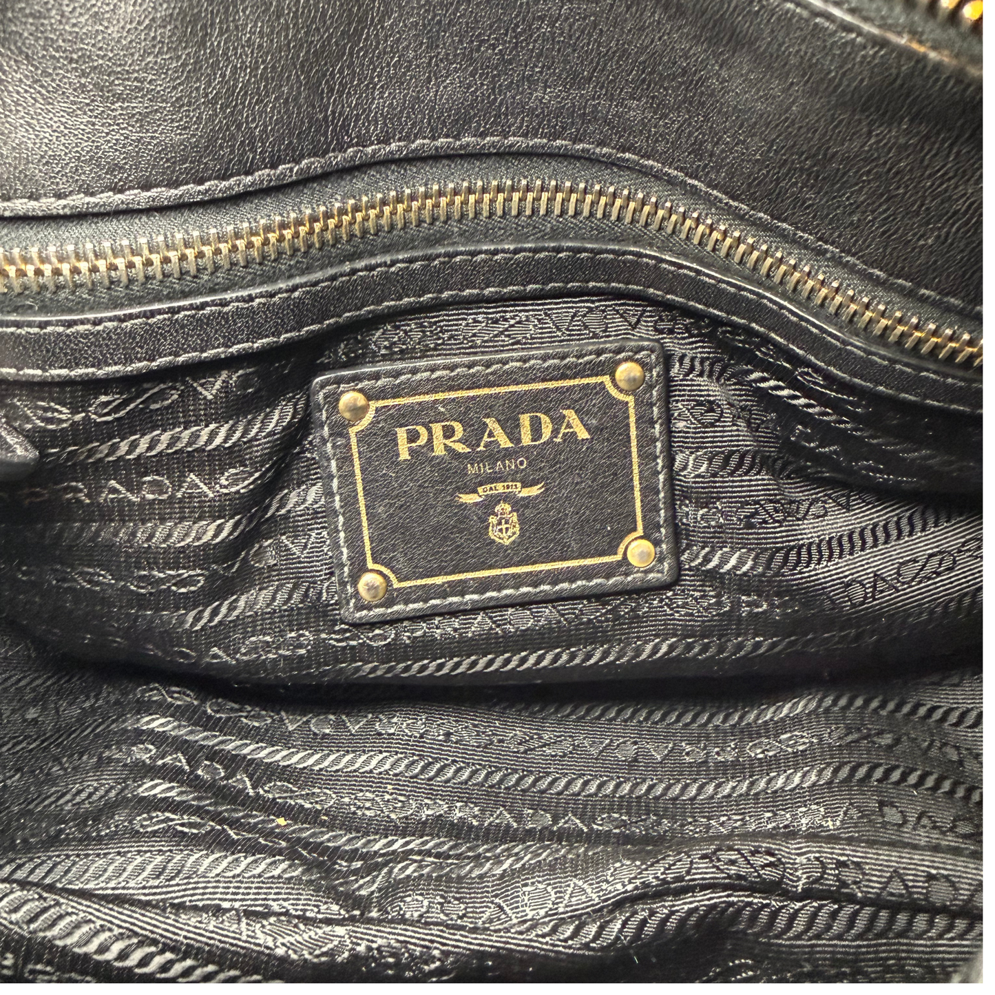 Close-up of a Prada handbag with gold zipper and logo.