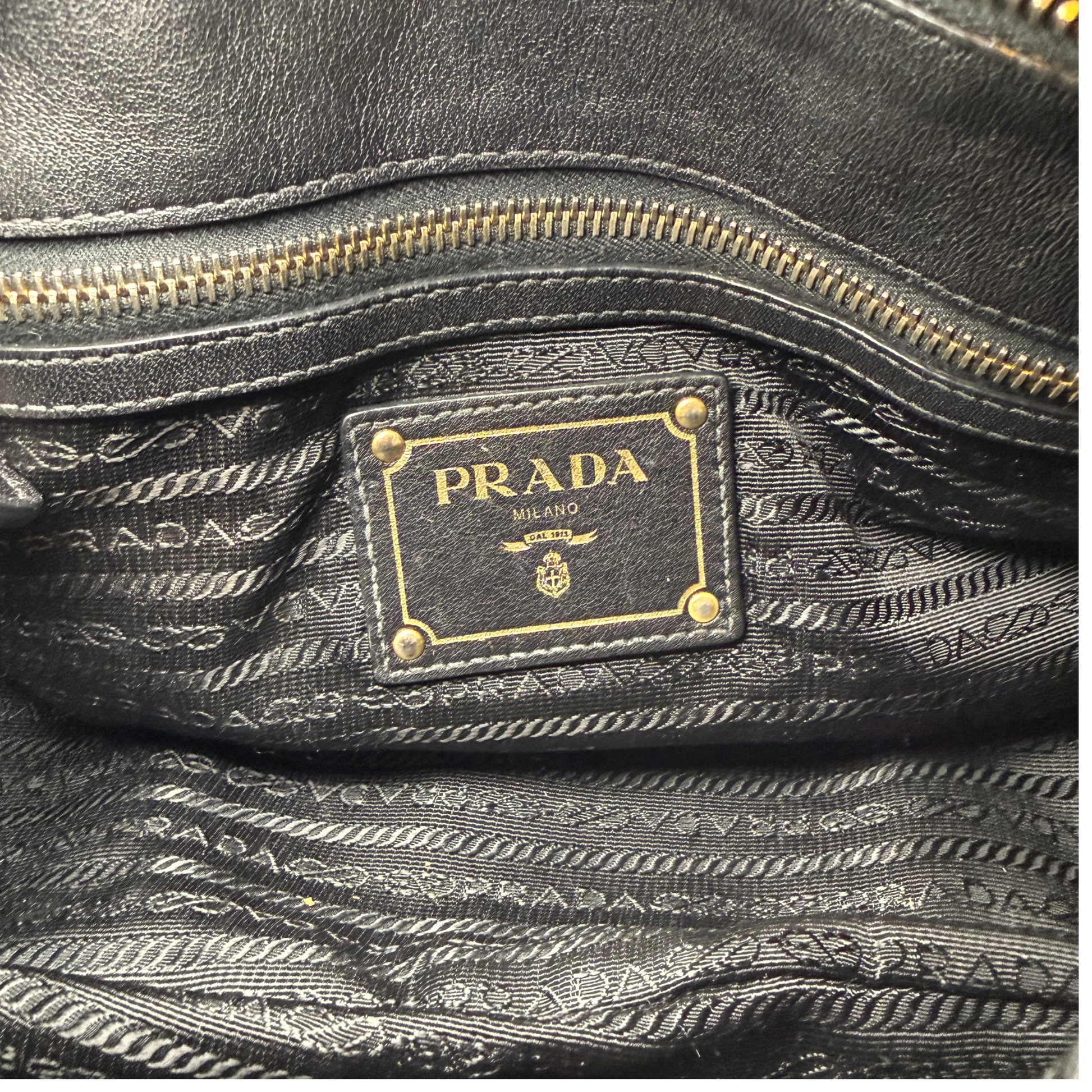 Close-up of a Prada handbag with gold zipper and logo.